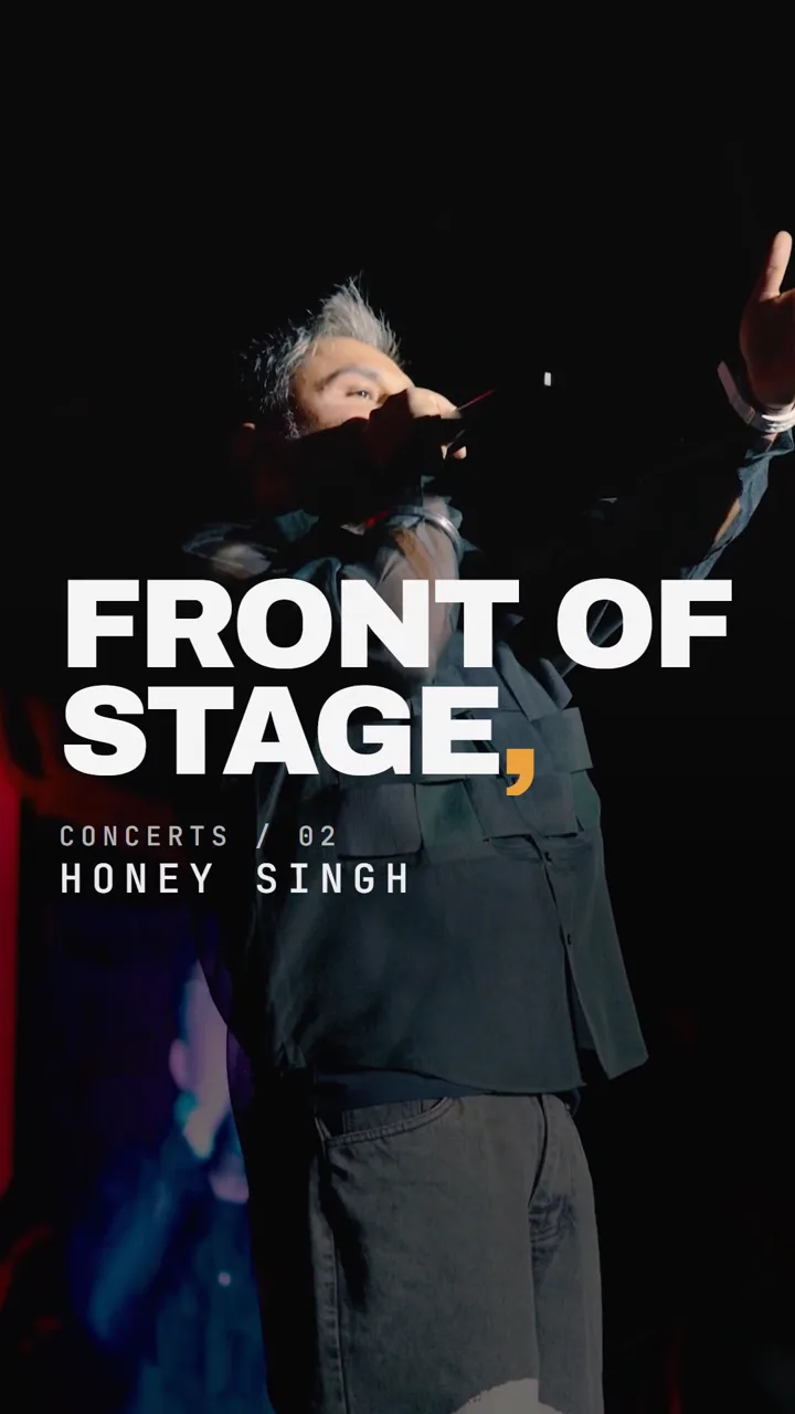 Still from the reel: a performer on a dark concert stage, mic raised, under heavy white caps reading “Front of stage,” with an amber comma